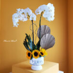Elegante orquídea con vibrantes girasoles en base Paris. - Image 2