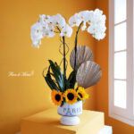 Elegante orquídea con vibrantes girasoles en base Paris.